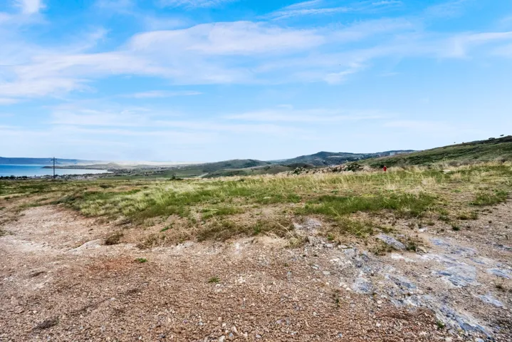 Expansive undeveloped land featuring natural terrain with scattered green foliage and distant water