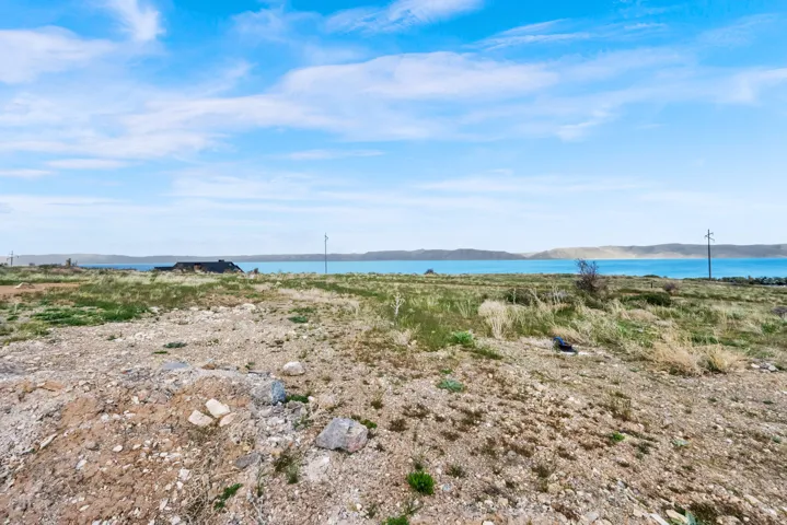Expansive land parcel featuring natural ground cover, distant water body, and distant hills