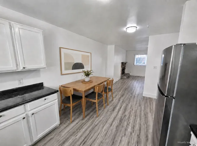 White cabinetry with dark countertops, wood-finish flooring, and a stone-clad fireplace