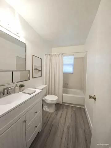 Vanity with white shaker-style cabinetry, wood-finish flooring, and a shower-tub combination