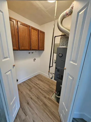 Laundry room with cabinet space, light wood-style floors, heating unit, hookup for a washing machine, and electric panel