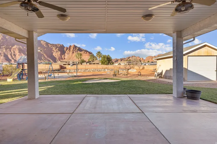 Fenced backyard with a ceiling fan, a playground, and a patio