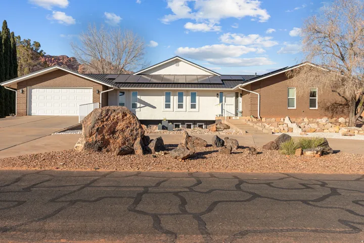 Single story home featuring roof mounted solar panels, brick siding, concrete driveway, and an attached garage