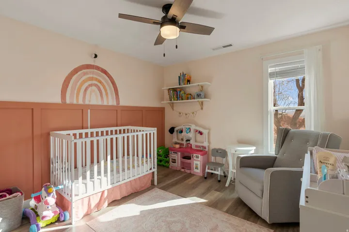 Bedroom featuring a crib, wood finished floors, ceiling fan, and a decorative wall