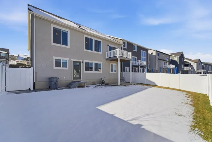 Back of property with a fenced backyard, a gate, stucco siding, a residential view, and a balcony