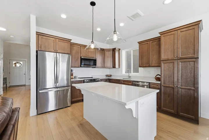 Kitchen featuring appliances with stainless steel finishes, pendant lighting, a kitchen island, light wood finished floors, and light stone counters