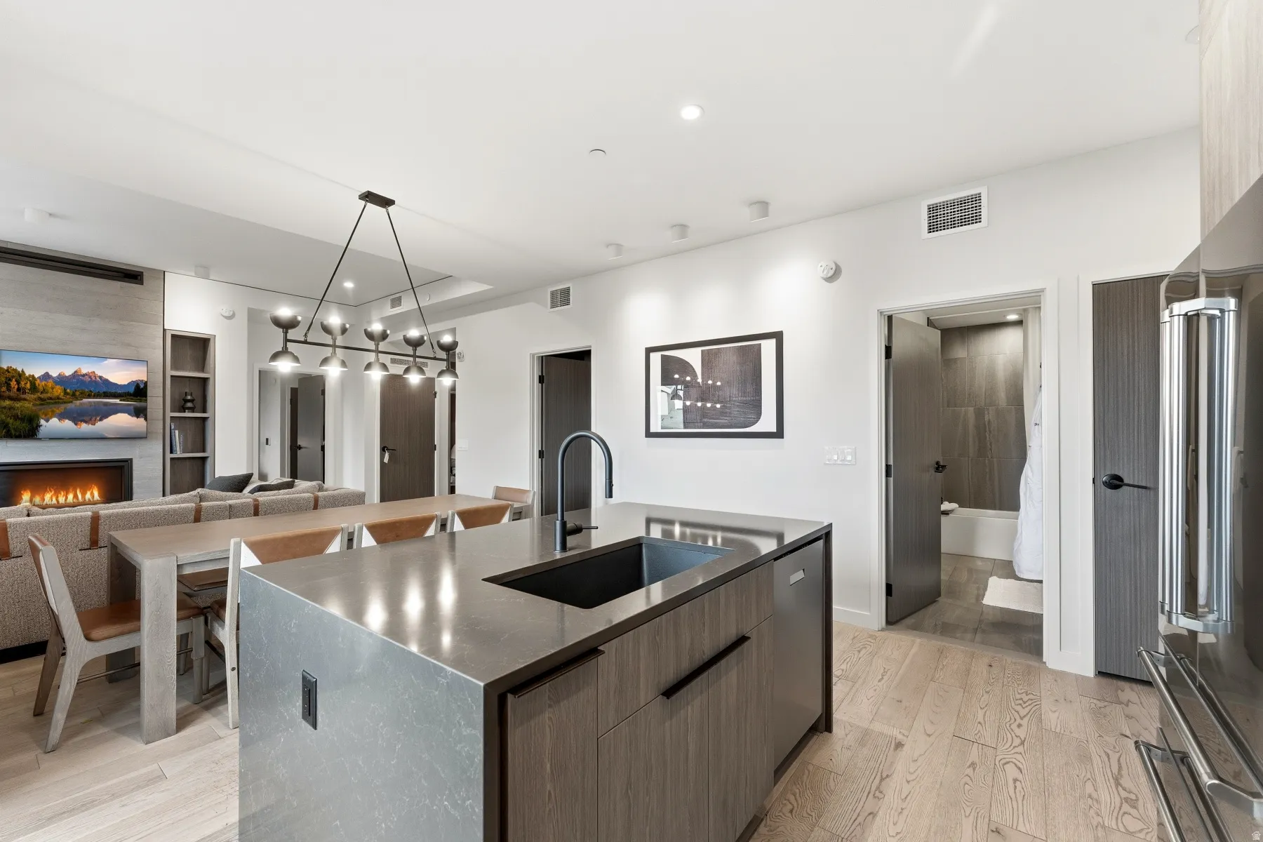 Kitchen with pendant lighting, a kitchen island with sink, modern cabinets, light wood-style floors, and high quality fridge