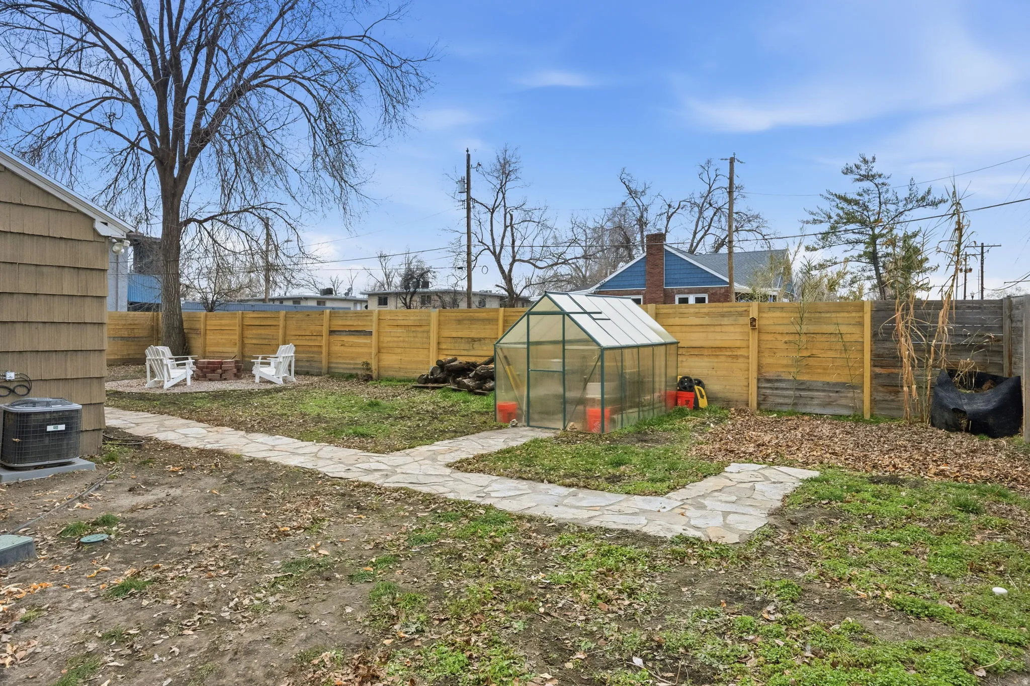 Fenced backyard featuring a greenhouse, an outdoor structure, an outdoor fire pit, and a patio