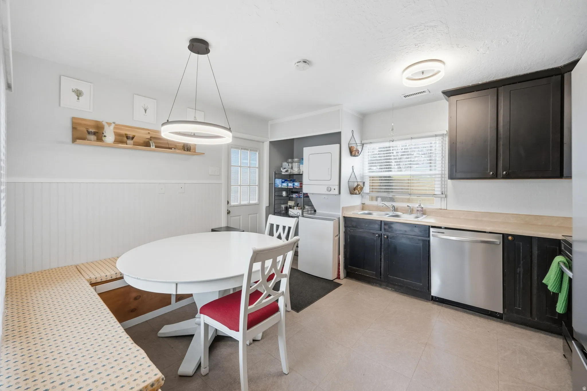 Kitchen with a wainscoted wall, light countertops, dishwasher, estacked washer and dryer, and hanging light fixtures