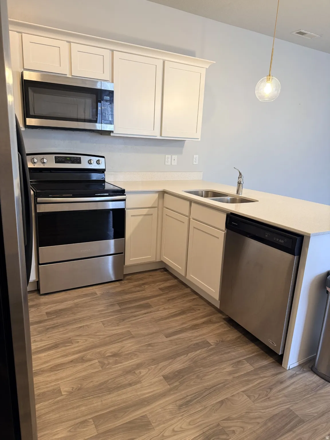 Kitchen with stainless steel appliances, pendant lighting, white cabinets, a peninsula, and dark wood finished floors
