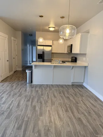 Kitchen with white cabinetry, a peninsula, light countertops, stainless steel appliances, and wood finished floors