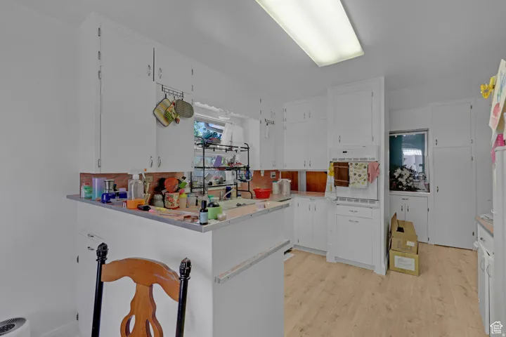 Kitchen with white cabinetry, white oven, light wood finished floors, light countertops, and a peninsula