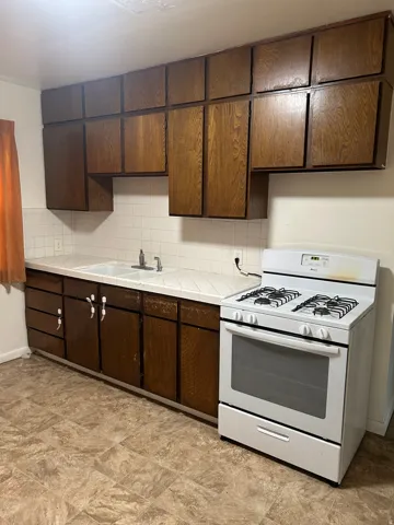 Kitchen with white gas stove, dark wood finish cabinets, stone finish flooring, and tile countertops