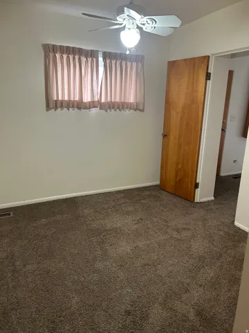 Unfurnished bedroom featuring dark carpet and ceiling fan
