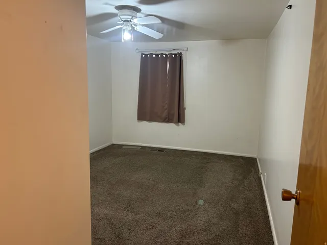 Unfurnished room featuring dark carpet and ceiling fan