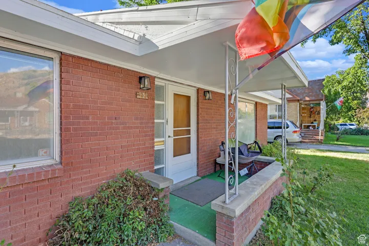 Entrance to property with covered porch, brick siding, and a lawn