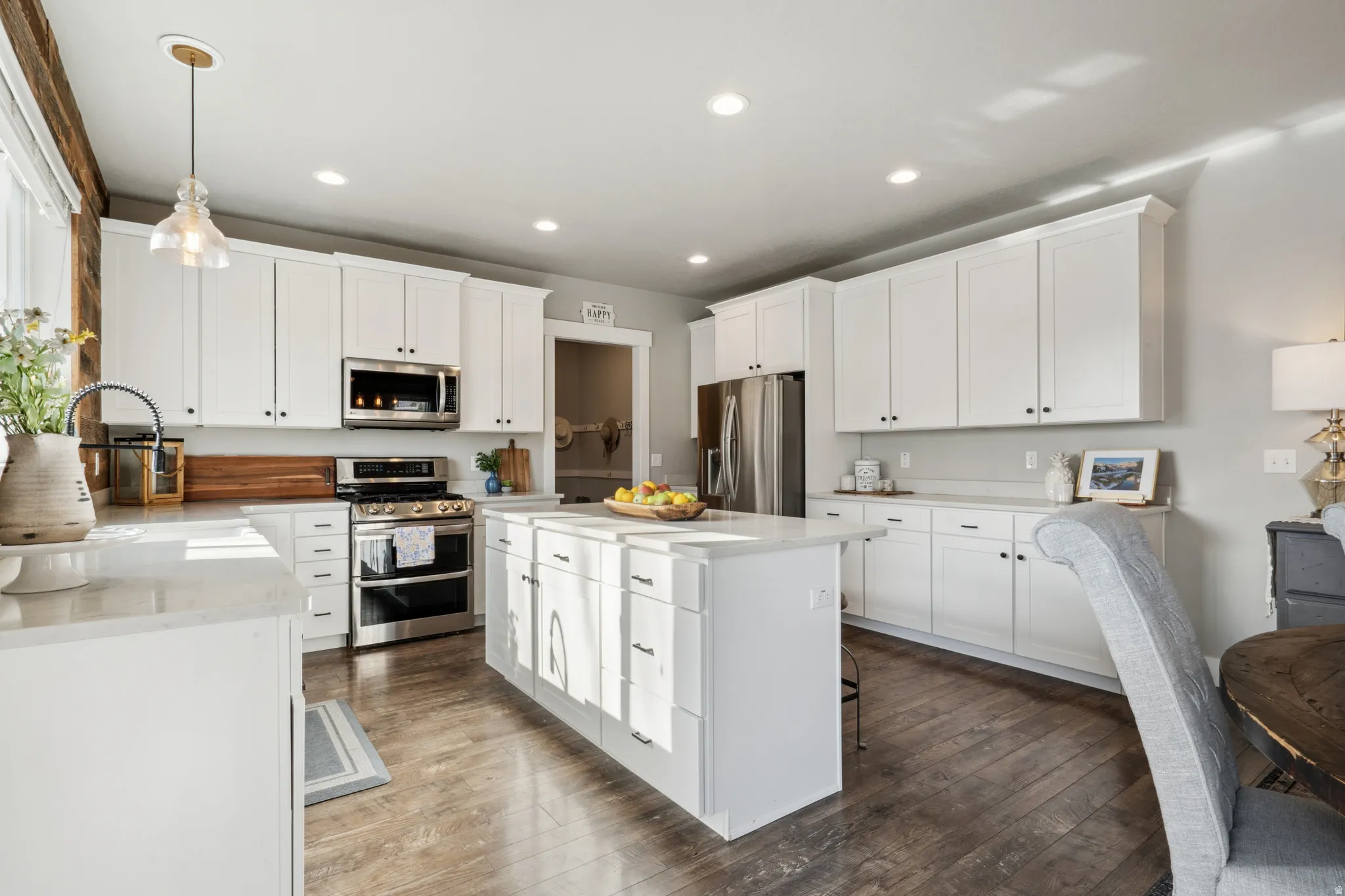 Kitchen featuring appliances with stainless steel finishes, pendant lighting, white cabinetry, dark wood finished floors, and light stone countertops