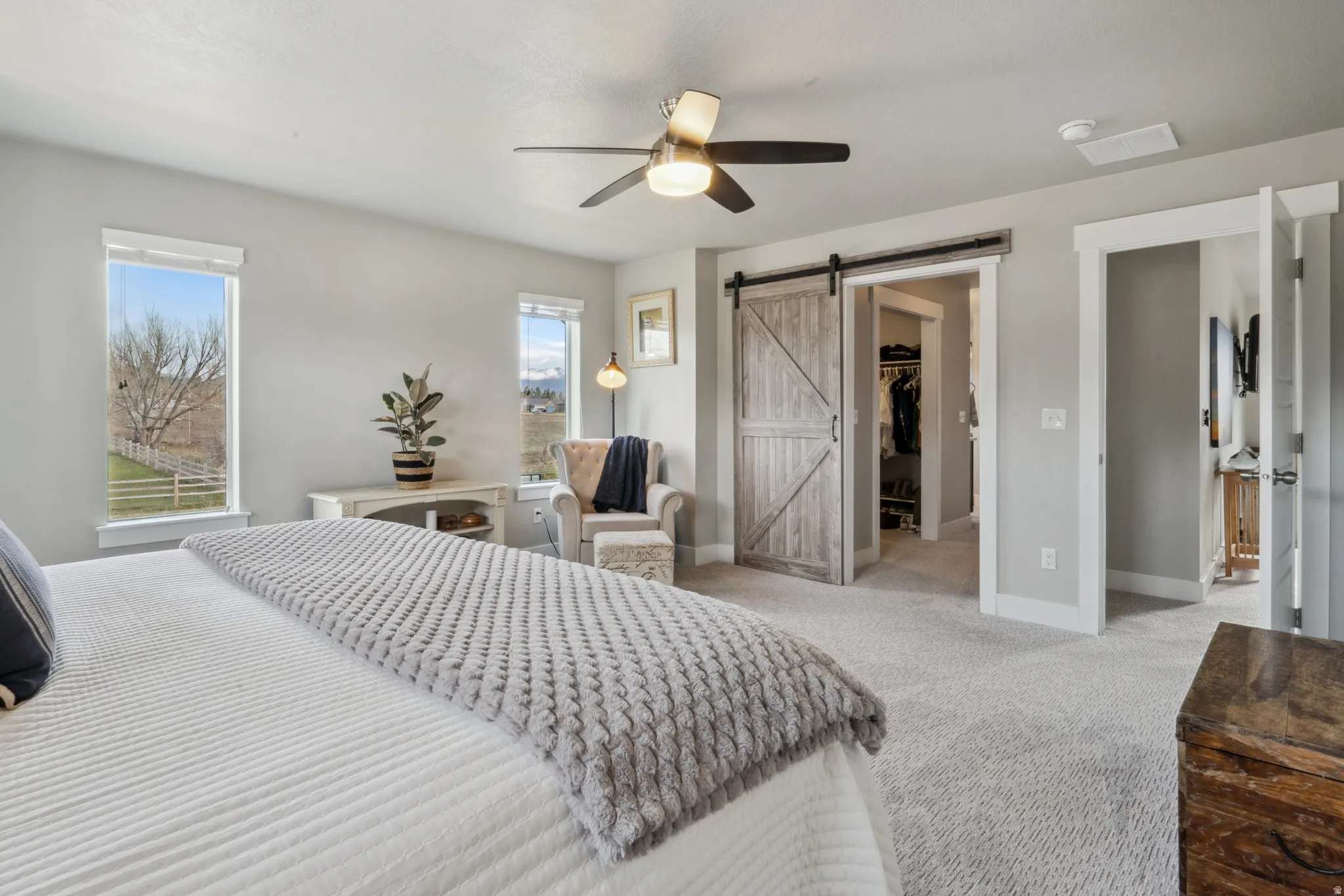Primary bedroom with a barn door, light colored carpet, a walk in closet, and ceiling fan