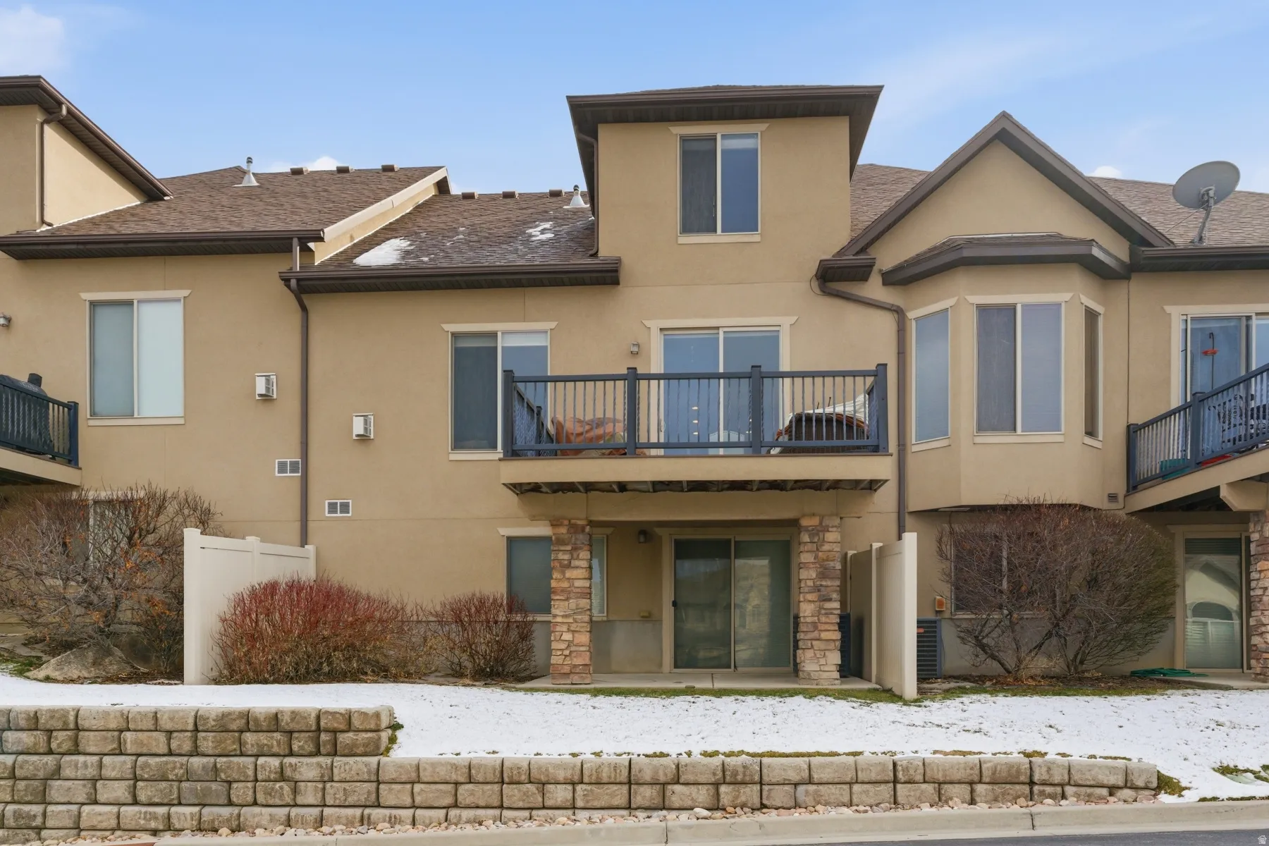 Rear view of property featuring stucco siding, roof with shingles, stone siding, and a patio area