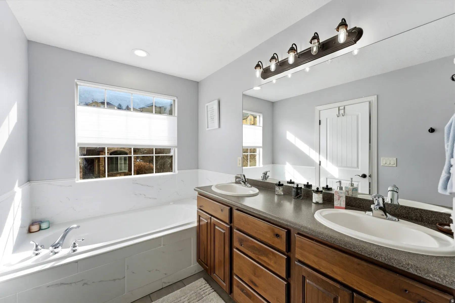 Full bath featuring double vanity, a bath, and healthy amount of natural light