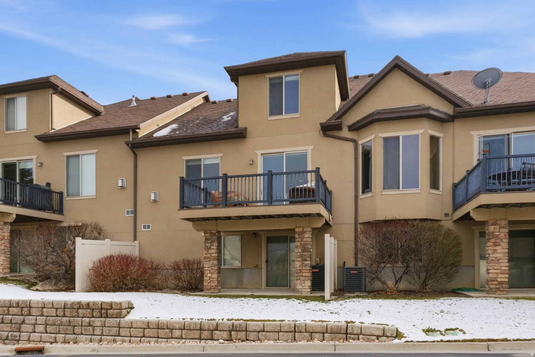 Back of house featuring stone siding, stucco siding, and a balcony