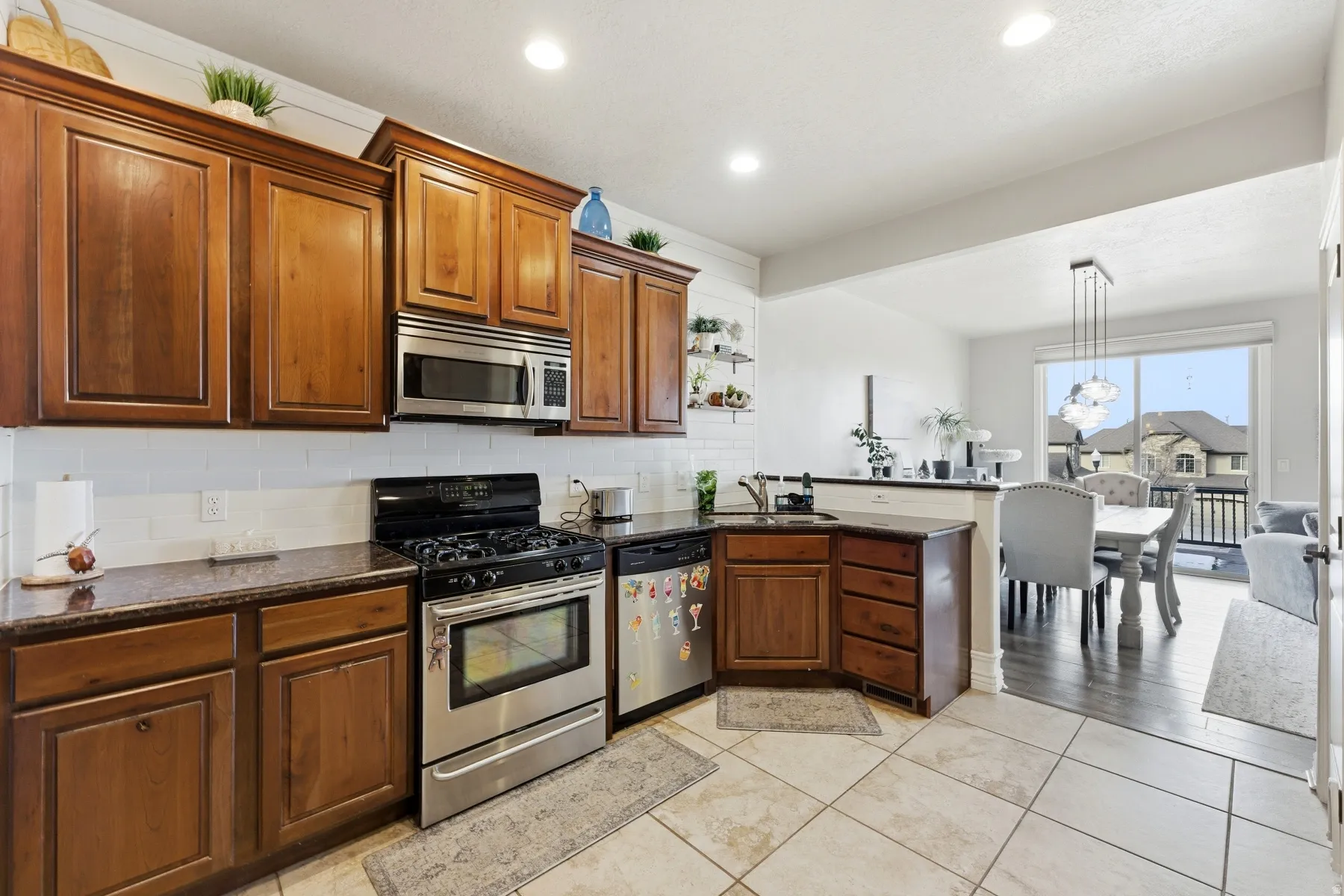 Kitchen featuring appliances with stainless steel finishes, a peninsula, dark stone counters, backsplash, and brown cabinetry