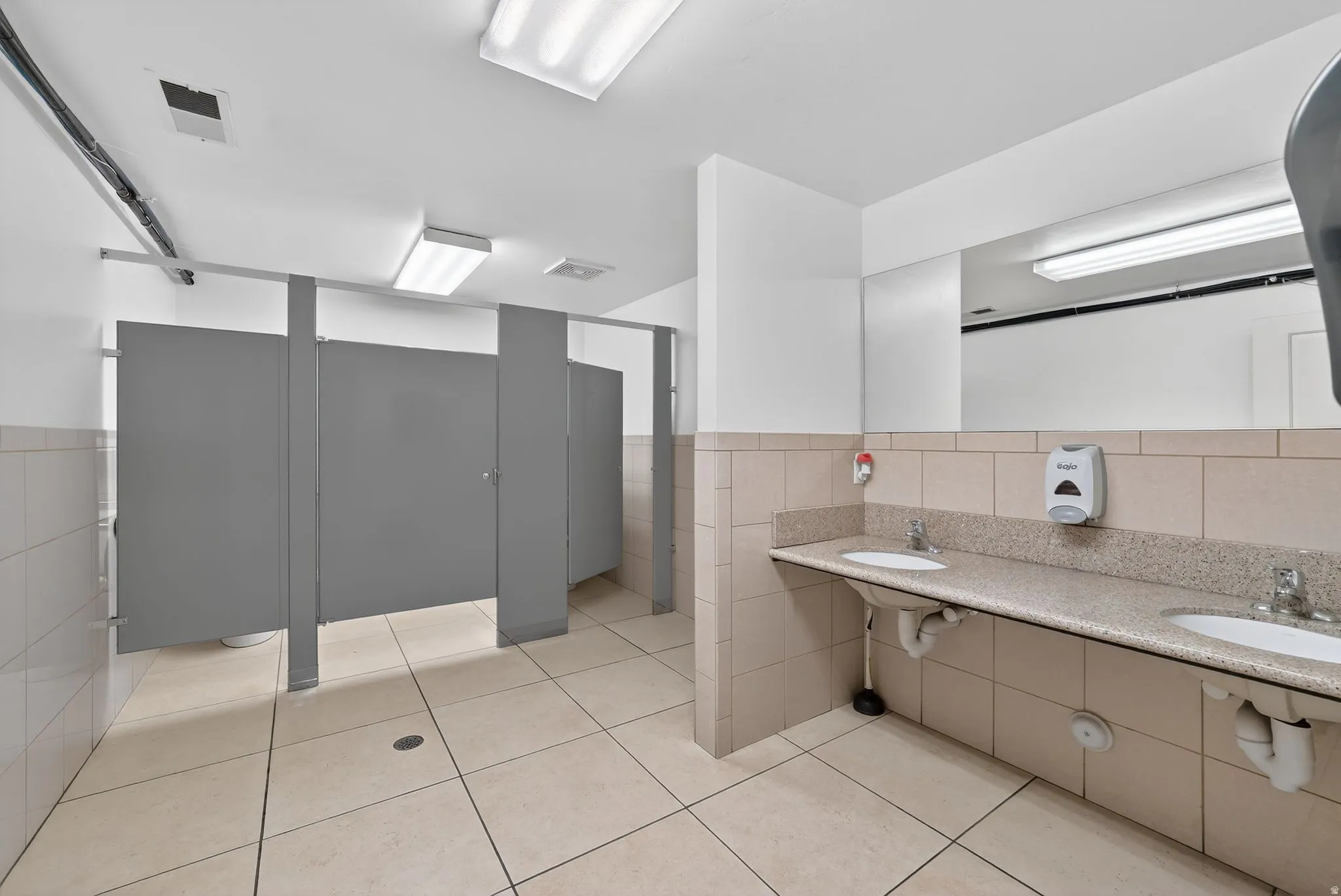 Full bathroom featuring tile walls, double vanity, wainscoting, and a shower stall