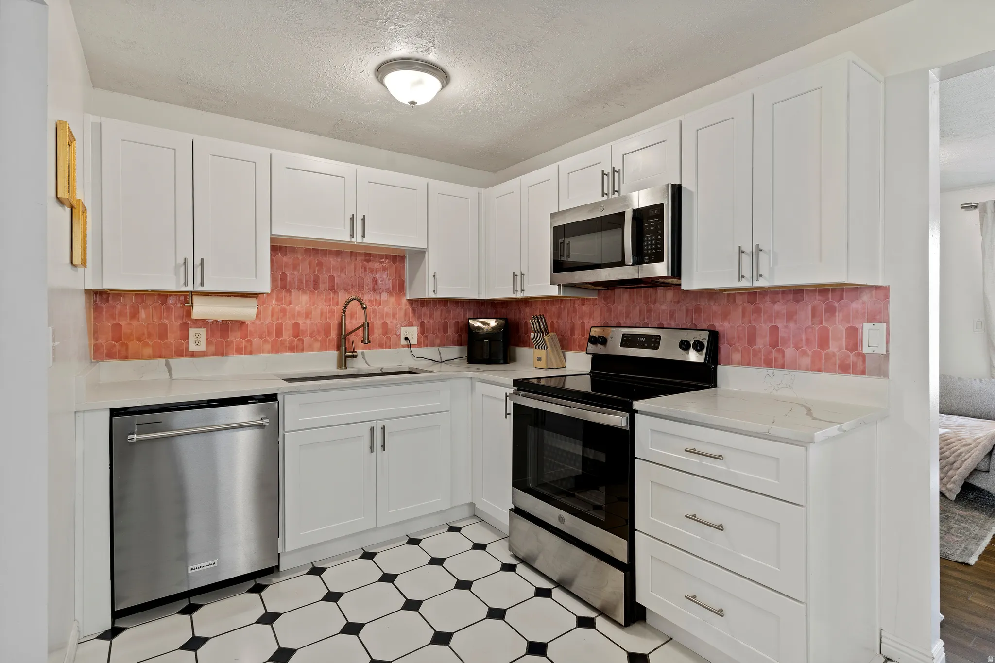 Kitchen with light floors, stainless steel appliances, white cabinets, and a textured ceiling