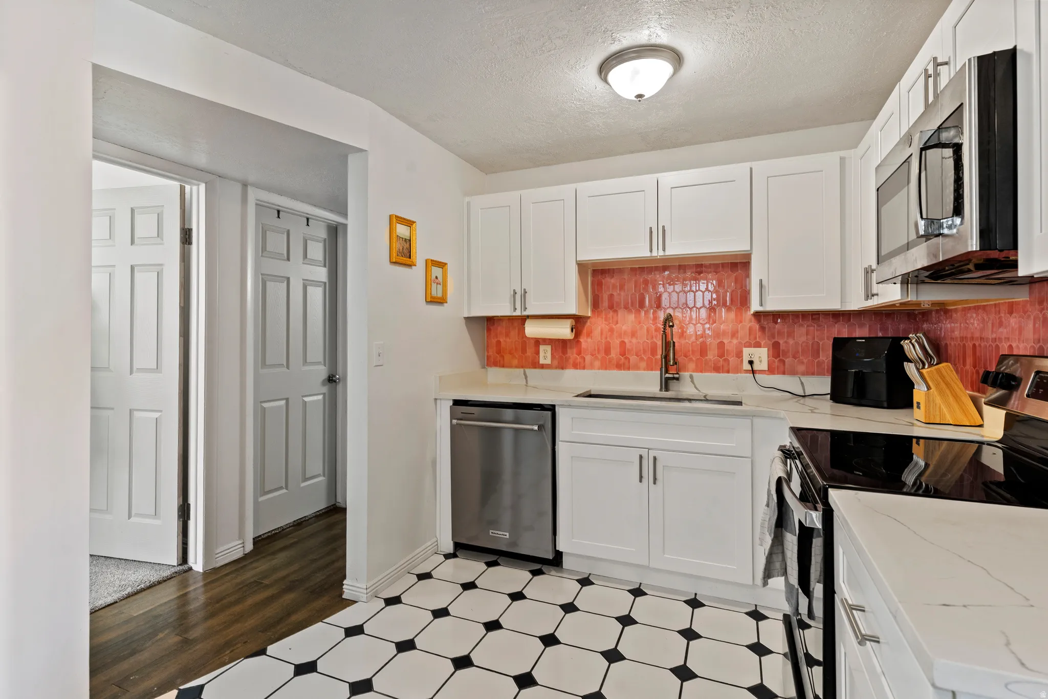 Kitchen featuring appliances with stainless steel finishes, white cabinetry, light flooring, a textured ceiling, and light stone counters