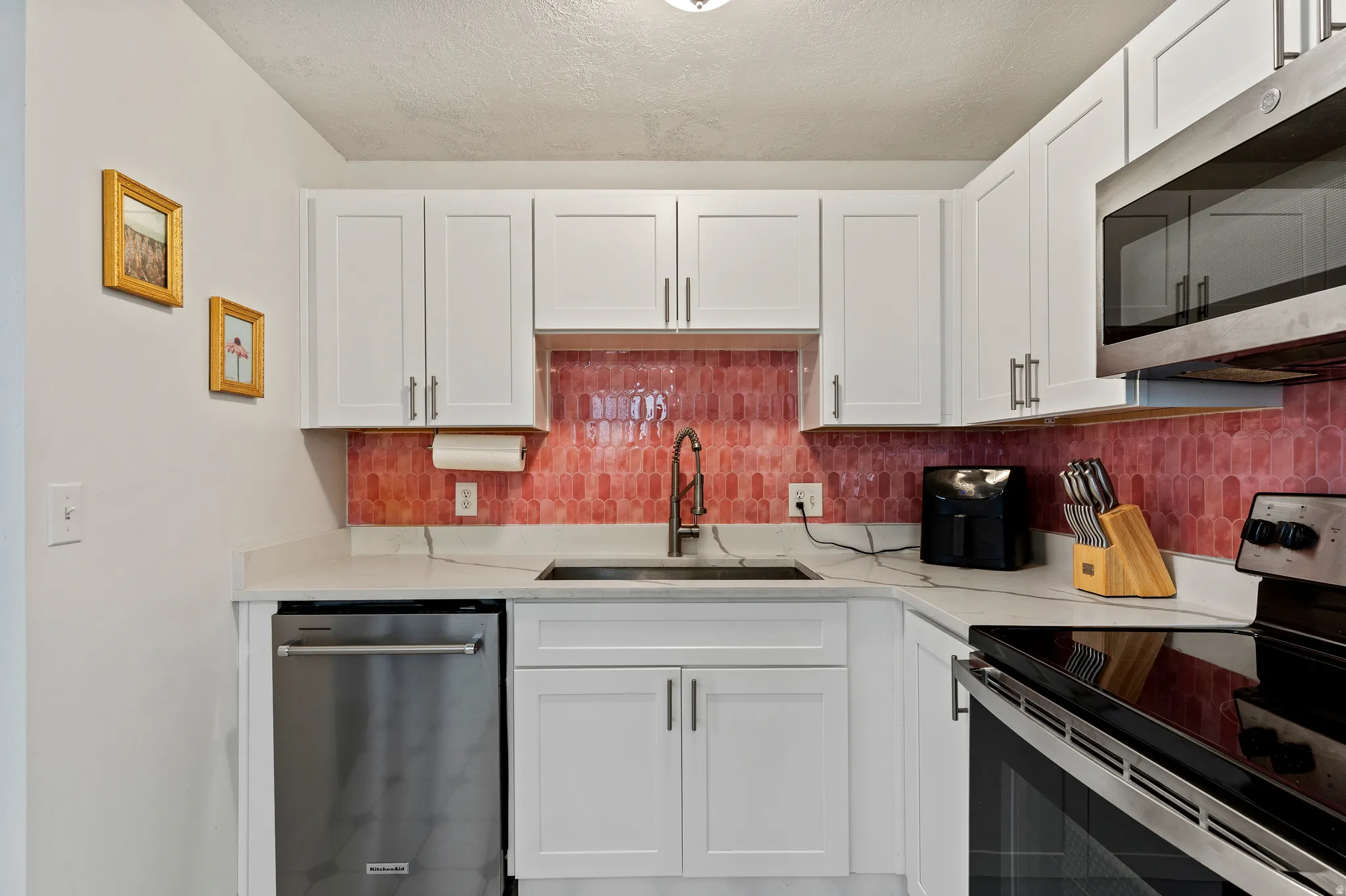 Kitchen with stainless steel appliances, white cabinets, light stone countertops, a textured ceiling, and tasteful backsplash