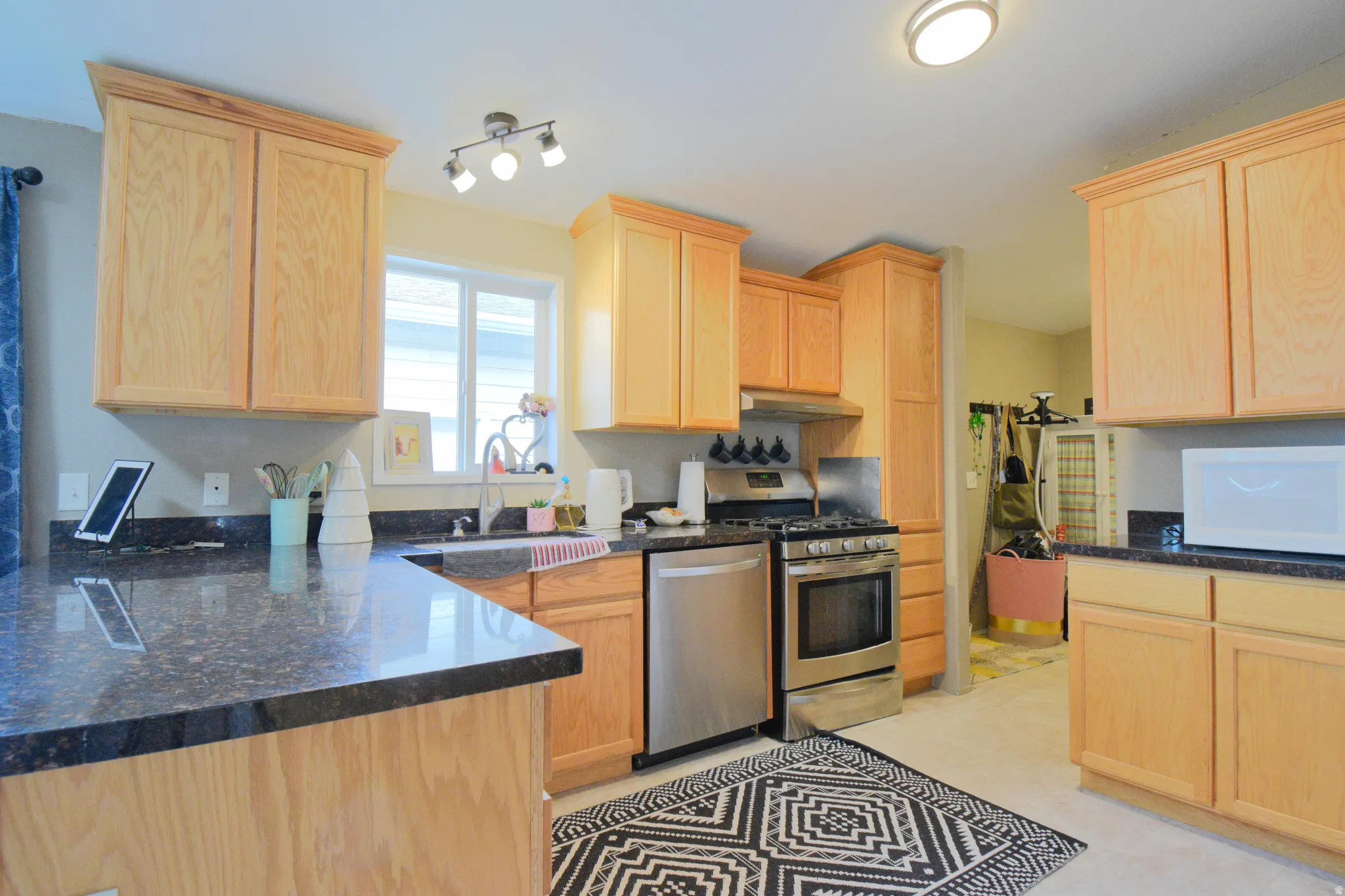 Kitchen with light brown cabinets, stainless steel appliances, dark Marble counters, and under cabinet range hood
