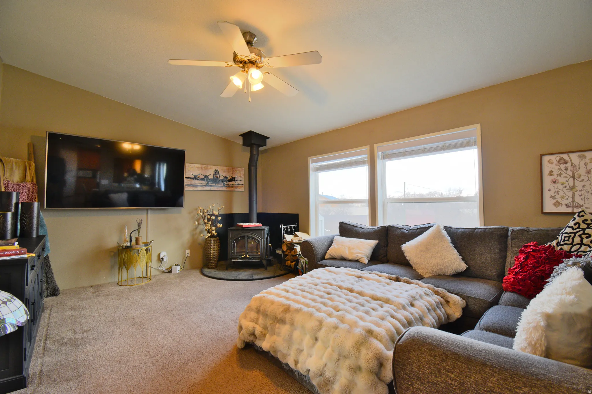 Living room featuring a wood stove, lofted ceiling, carpet, and a ceiling fan