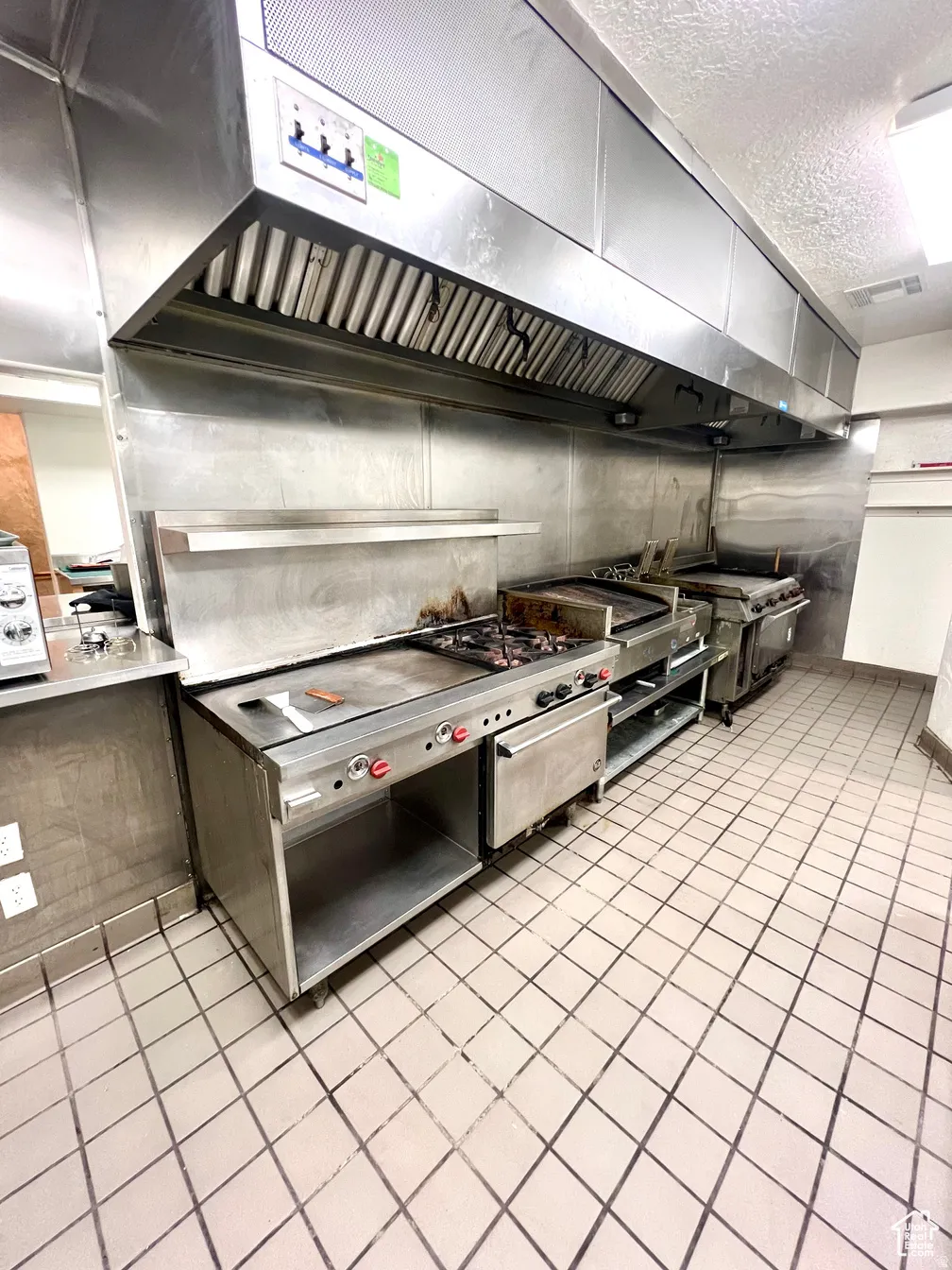 Kitchen with wall chimney exhaust hood, a textured ceiling, and stainless steel range oven