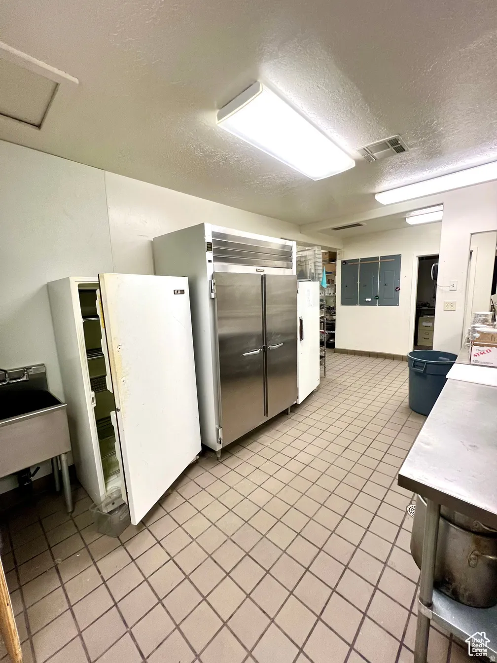 Kitchen with a textured ceiling, freestanding refrigerator, light countertops, built in refrigerator, and white cabinetry