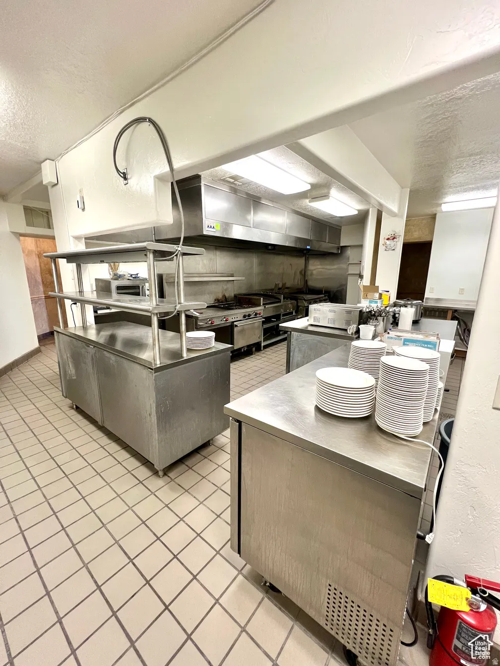 Kitchen with a textured ceiling, wall chimney range hood, a textured wall, stainless steel counters, and stainless steel stove