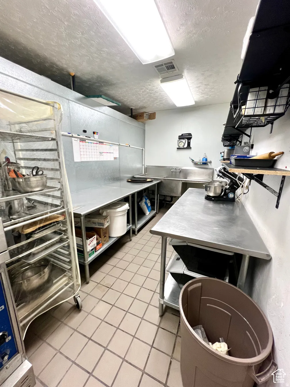Kitchen with stainless steel countertops, a textured ceiling, and open shelves