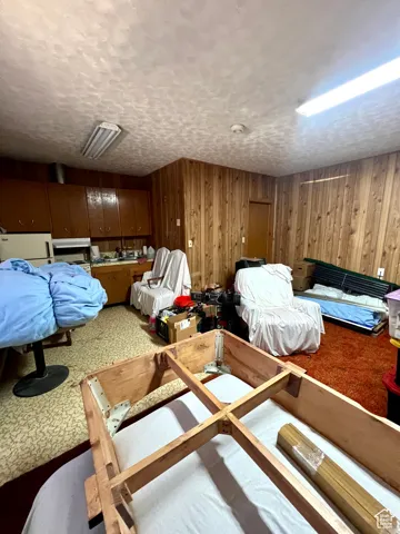 Bedroom featuring a textured ceiling, wood walls, freestanding refrigerator, and carpet flooring