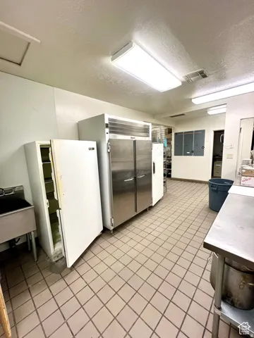 Kitchen with a textured ceiling, freestanding refrigerator, light countertops, built in refrigerator, and white cabinetry