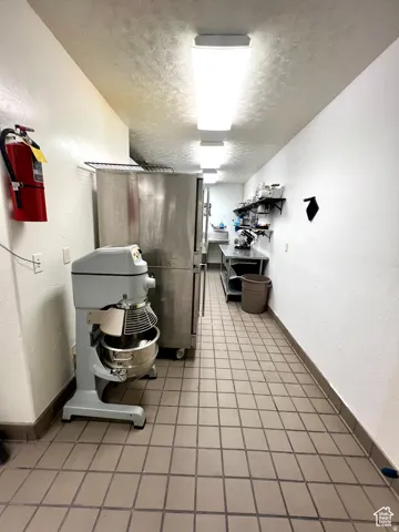 Kitchen featuring a textured ceiling, a textured wall, stainless steel refrigerator, and open shelves