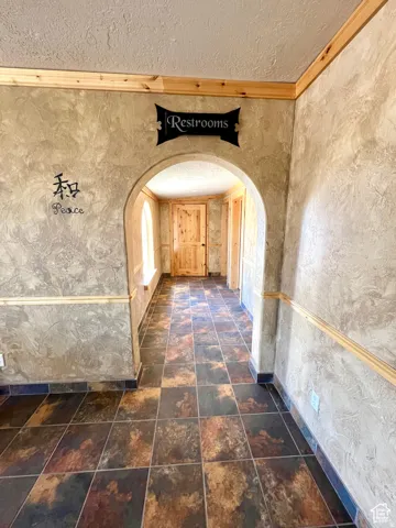 Corridor featuring a textured ceiling, ornamental molding, and arched walkways