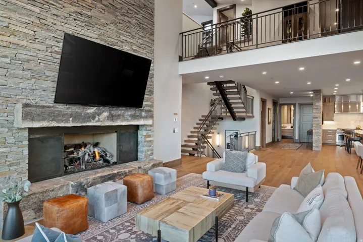 Living room with wood finished floors, a stone fireplace, recessed lighting, stairs, and a towering ceiling