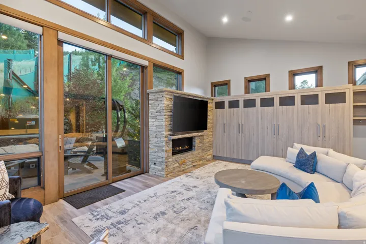 Living room featuring light wood-style flooring, a stone fireplace, plenty of natural light, and high vaulted ceiling