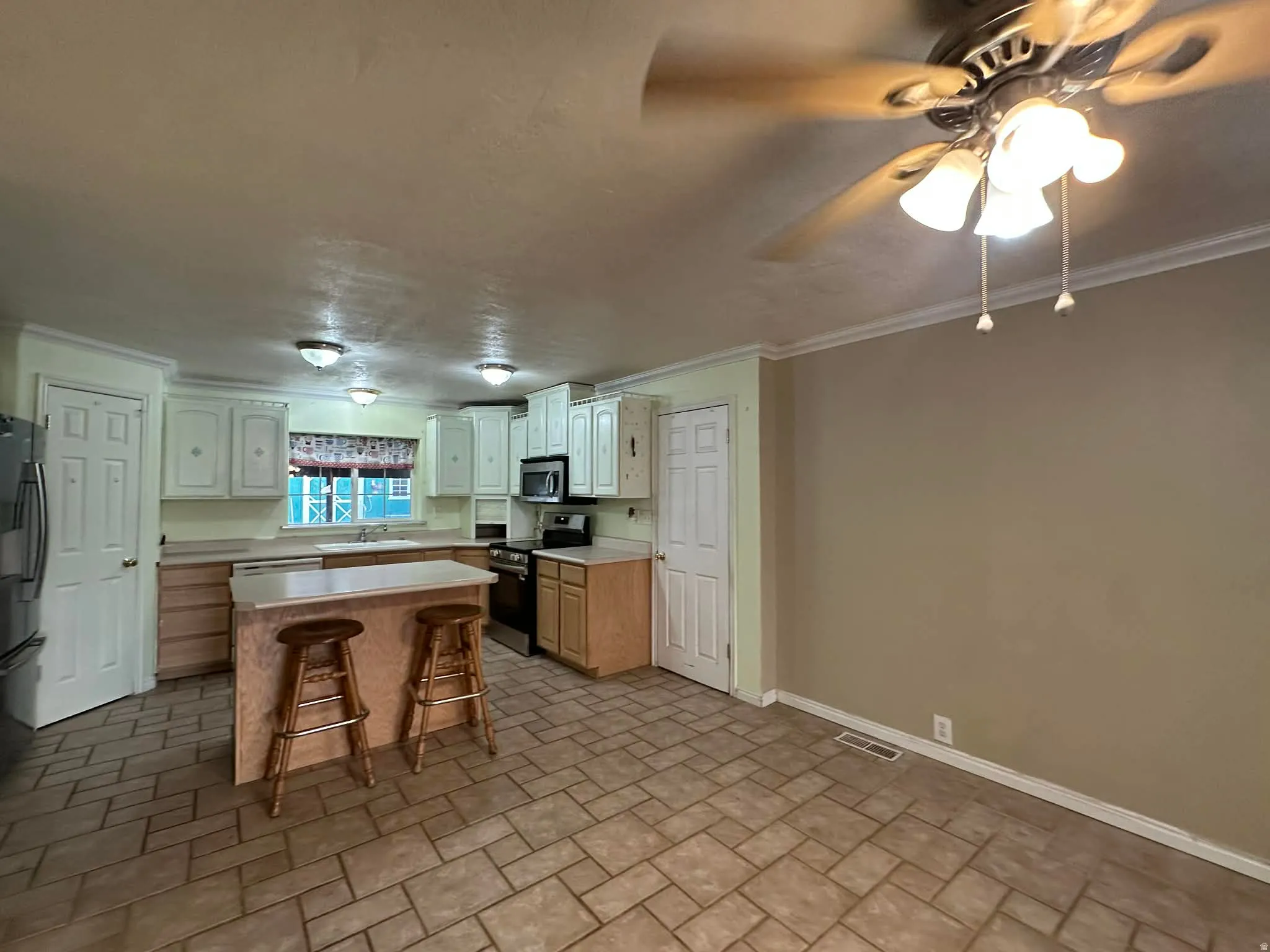 Kitchen featuring a breakfast bar, light countertops, stainless steel appliances, ornamental molding, and a kitchen island