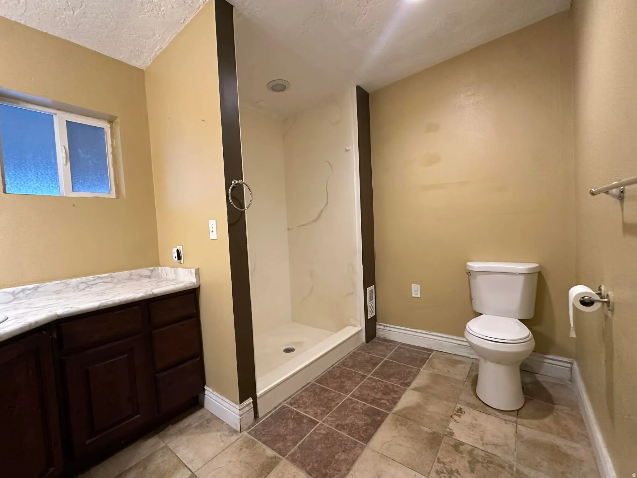 Primary bathroom with a textured ceiling, vanity, and a marble finish shower