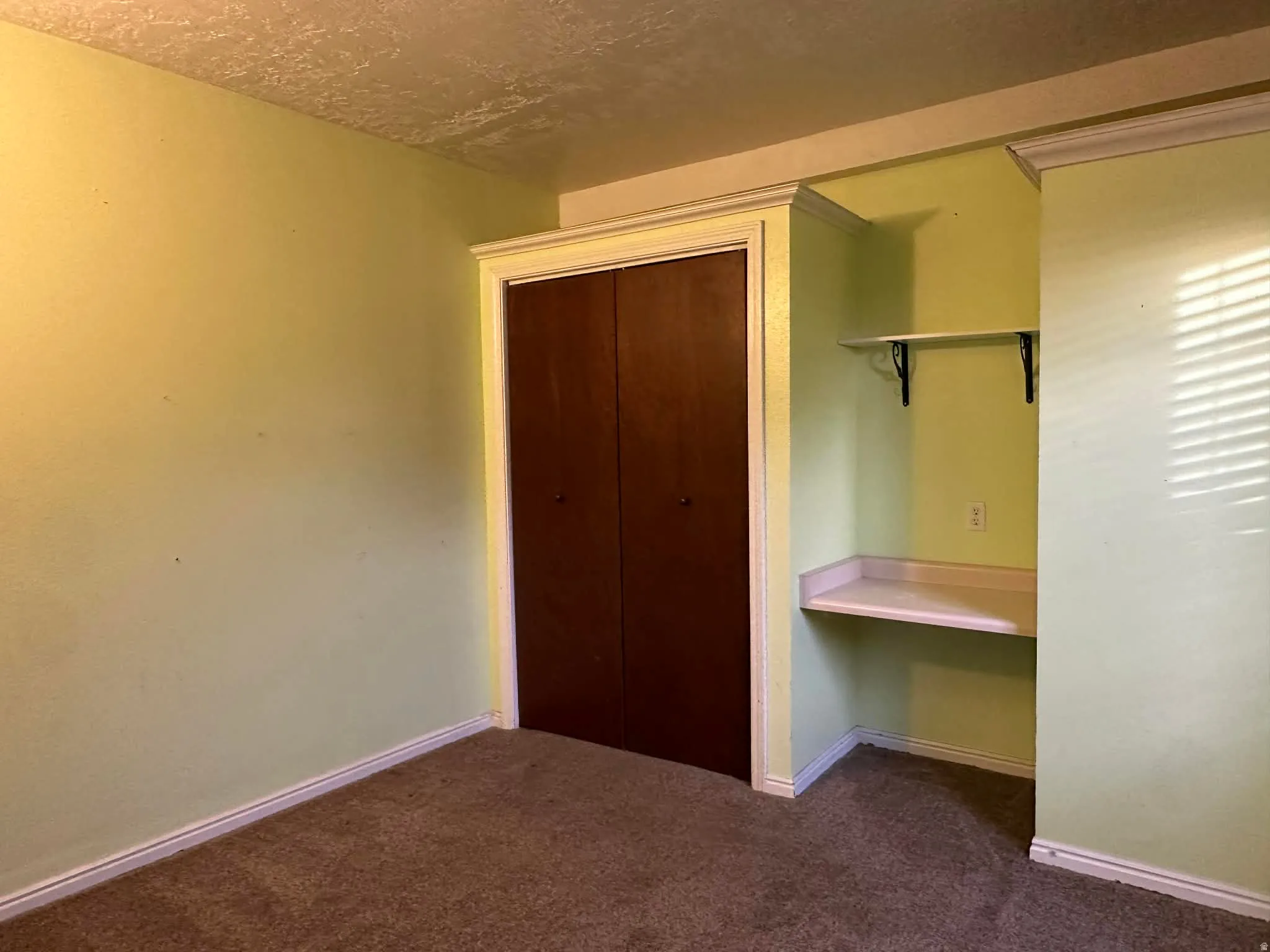 Unfurnished bedroom featuring a closet, dark colored carpet, a textured ceiling, and built in study area