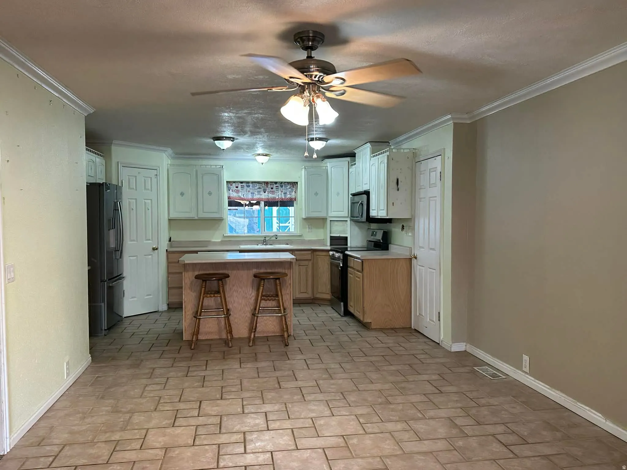 Kitchen with ceiling fan, electric range, light countertops, a kitchen breakfast bar, and stainless steel fridge