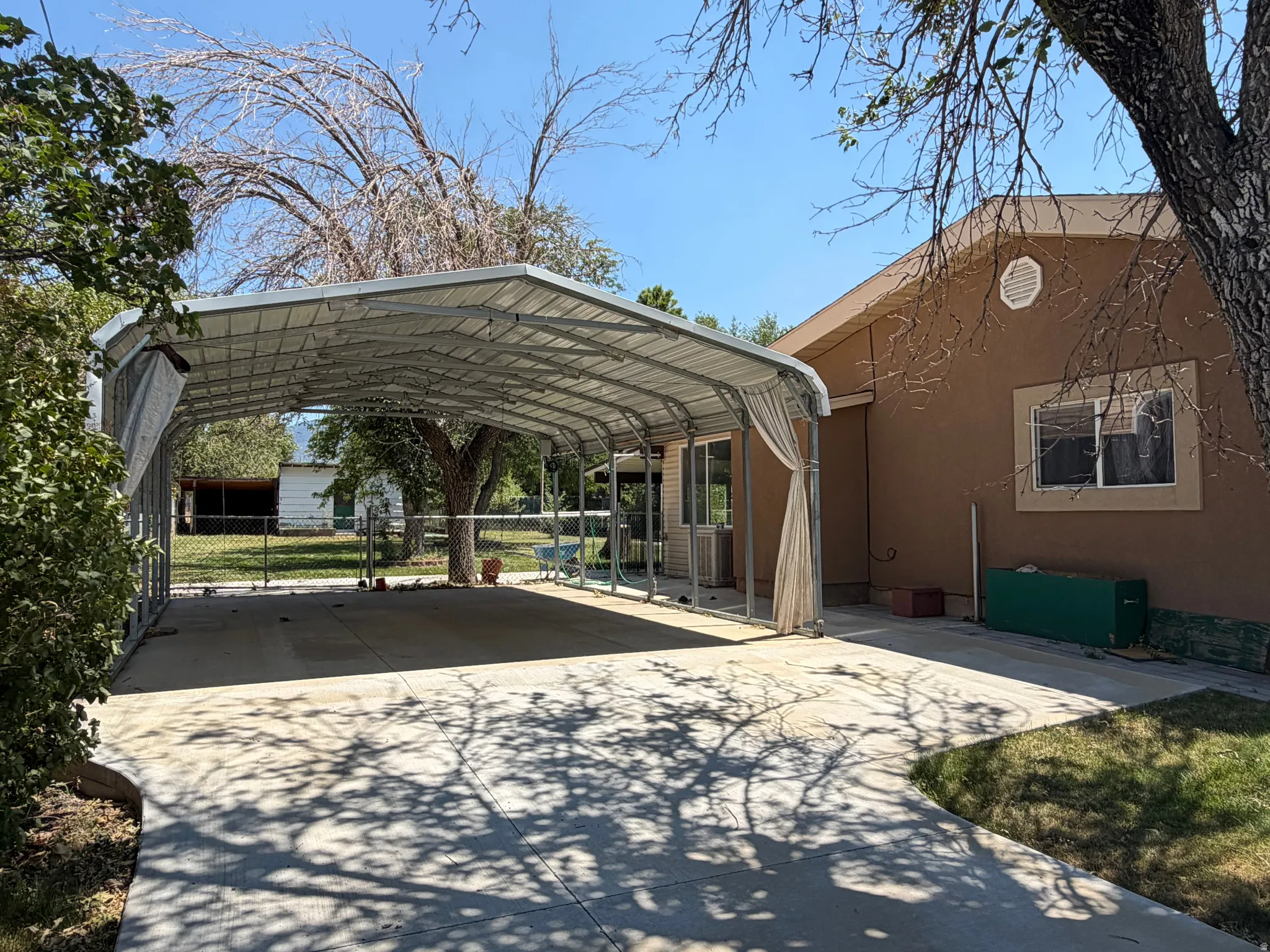 Spacious concrete driveway featuring an attached metal carport, providing covered parking and direct access to the stucco-sided residence