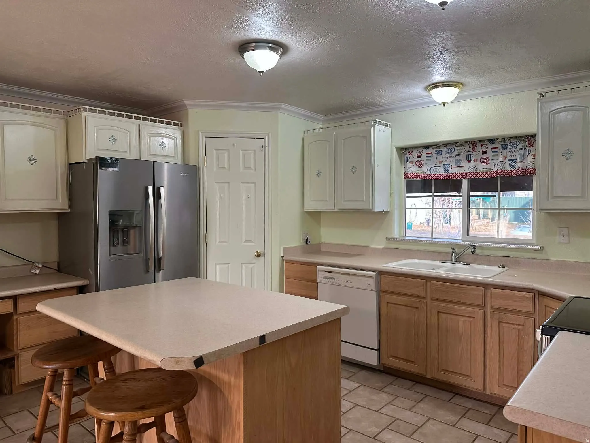 Kitchen with a textured ceiling, stainless steel fridge, a breakfast bar area, light countertops, and a kitchen island