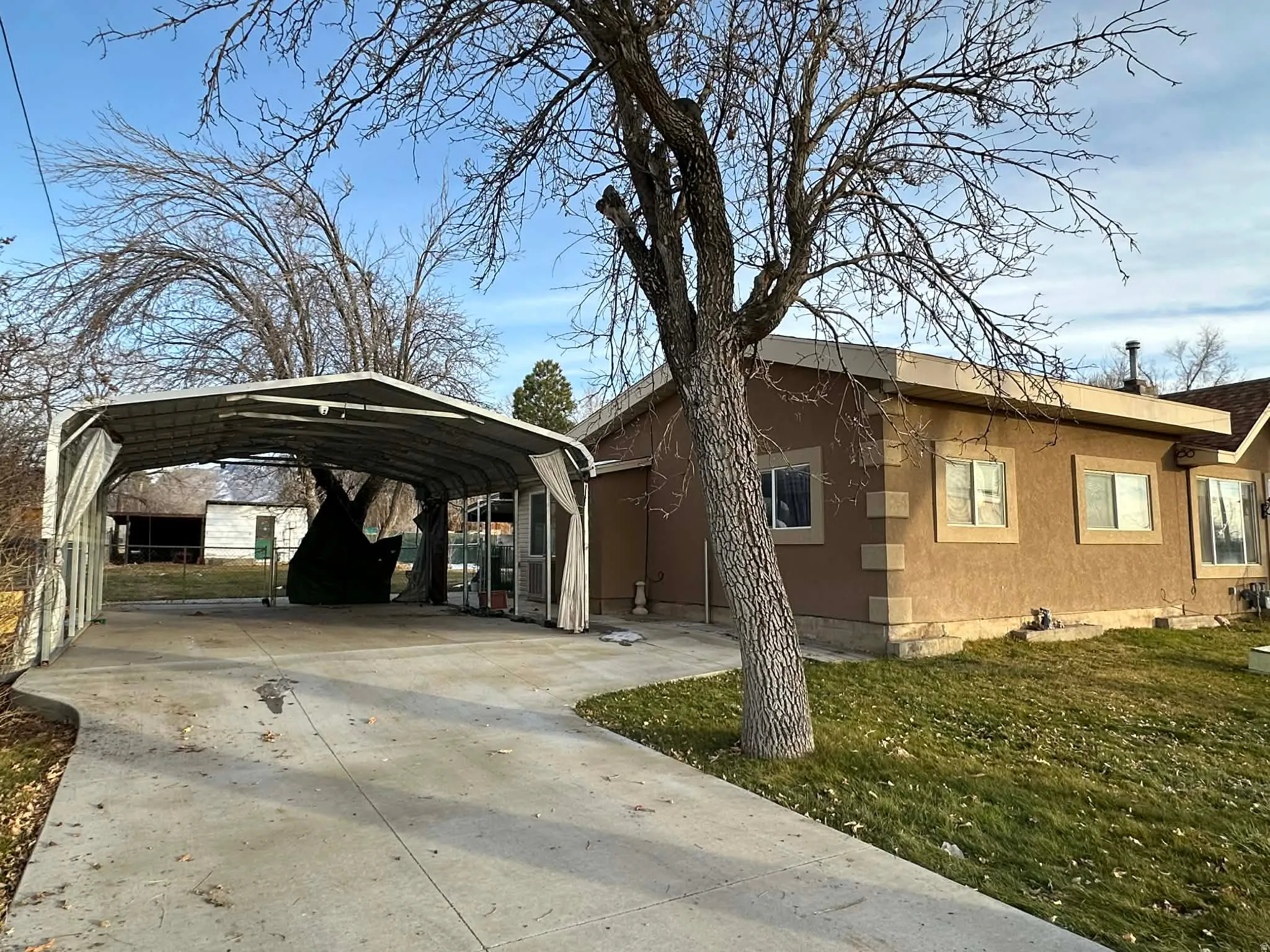 View of home's exterior featuring concrete driveway, a carport, stucco siding, and a lawn