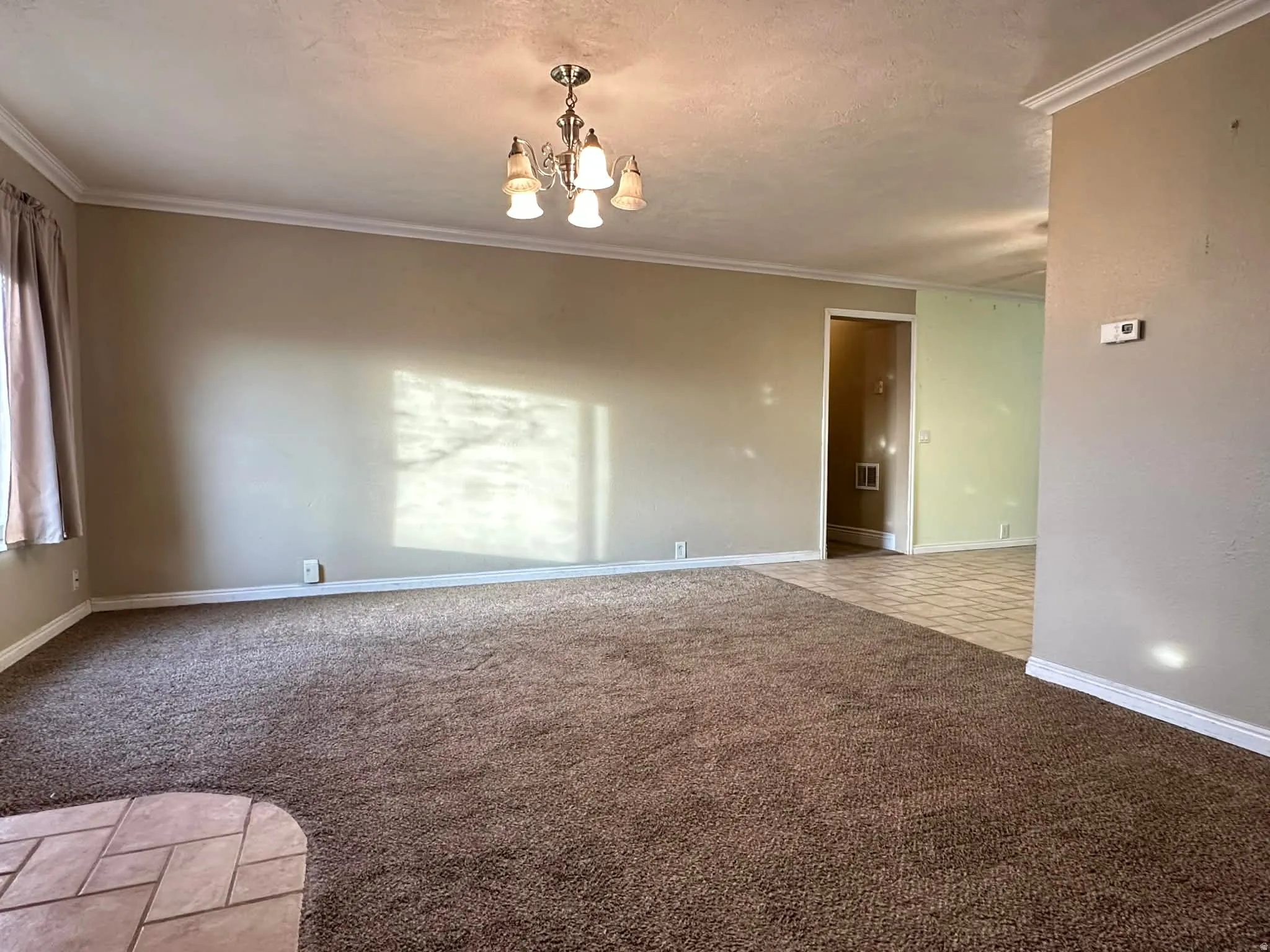 Spare room with light colored carpet, ornamental molding, a chandelier, and a textured ceiling